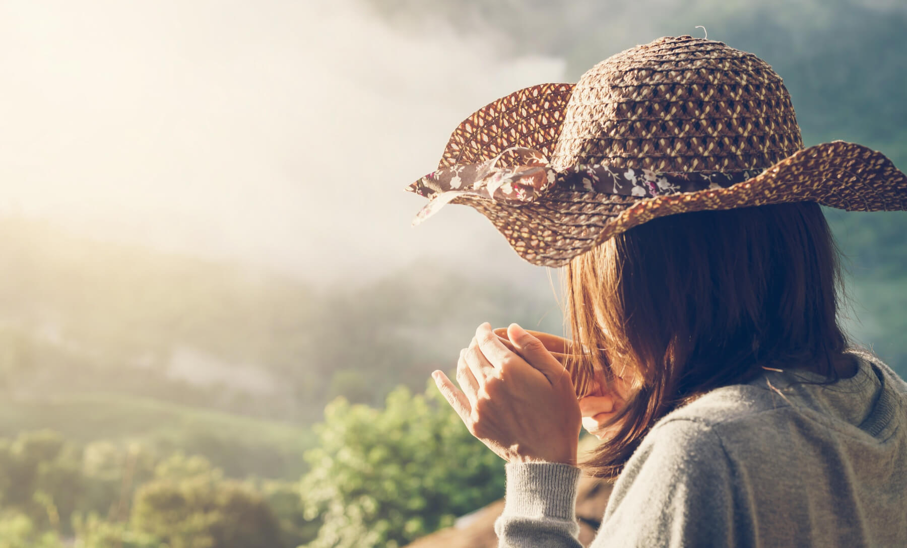 Eine Frau mit einem Sonnenhut hält eine Tasse nachhaltigen MAYOLA Kaffee aus Hattingen in den Händen und blickt in die sonnige Landschaft